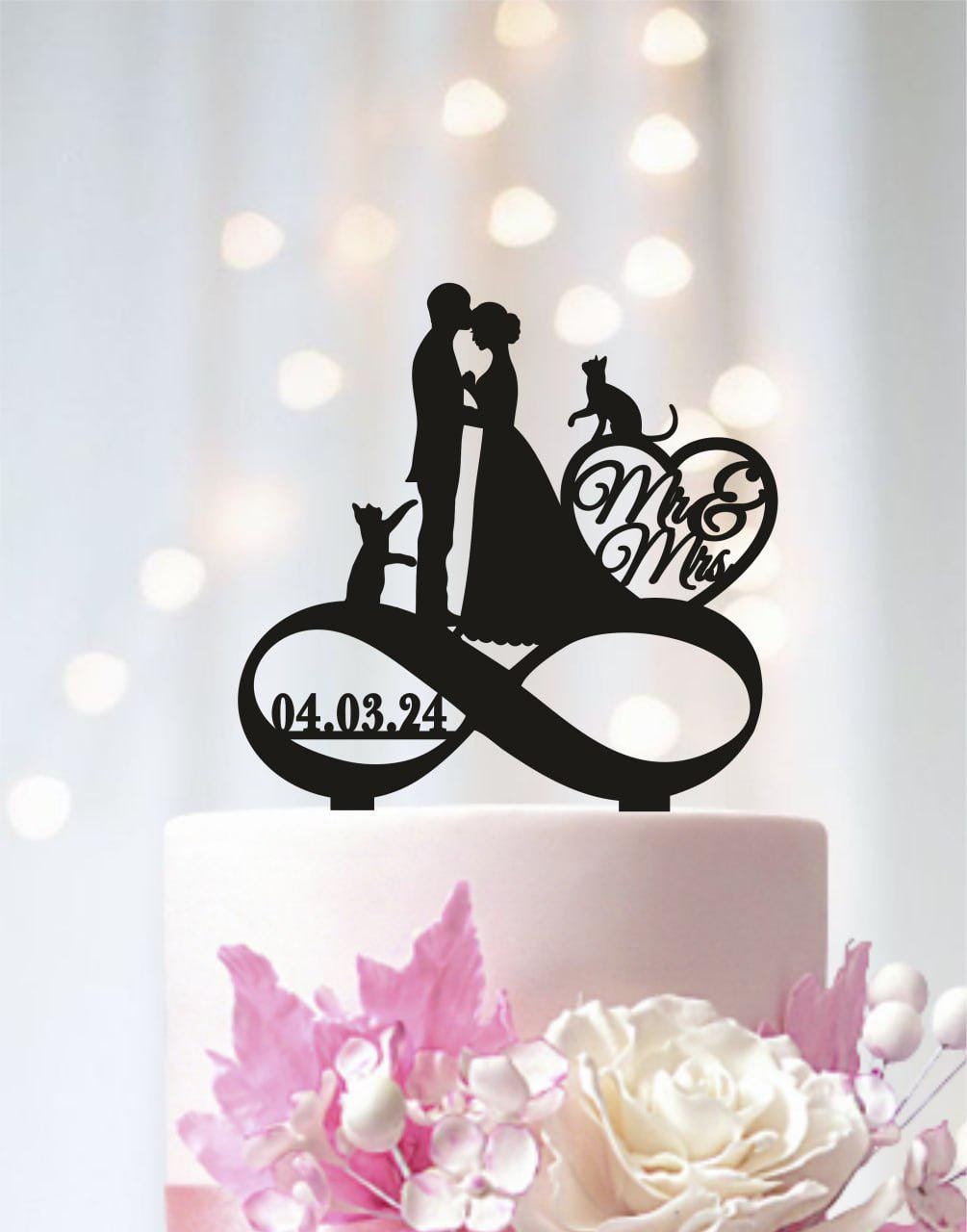 A black silhouette of a bride and groom on a wedding cake topper, with a heart-shaped decoration and the words "Mr & Mrs" written on it.