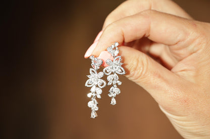 A hand holding a pair of elegant diamond earrings.