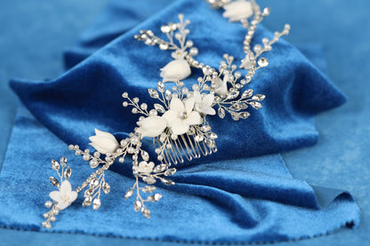 A close-up view of a decorative hair accessory, possibly a hair clip or headband, adorned with white flowers and sparkling crystals, resting on a blue velvet background.