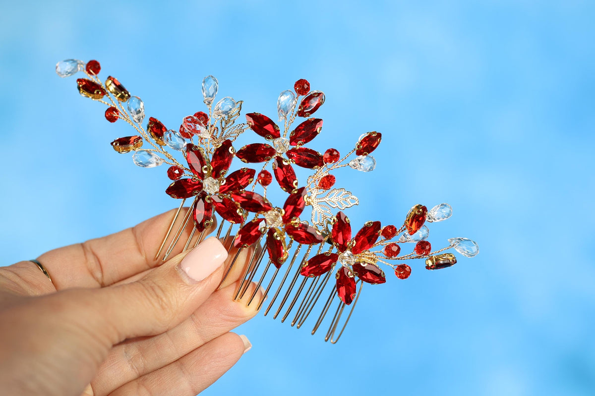A hand holding a decorative hair accessory with red and gold gemstones against a blue background.
