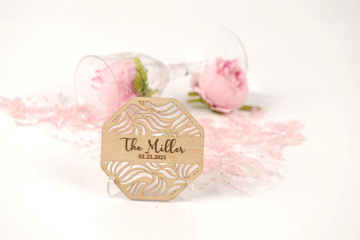 A wooden sign with the name "The Miller" and the date "02.23.2005" is placed in front of a glass with pink roses, along with some pink flowers scattered around.