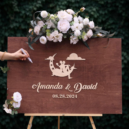 A wooden sign with a floral arrangement and a silhouette of a couple, along with the text "Amanda & David" and the date "08.28.2024".