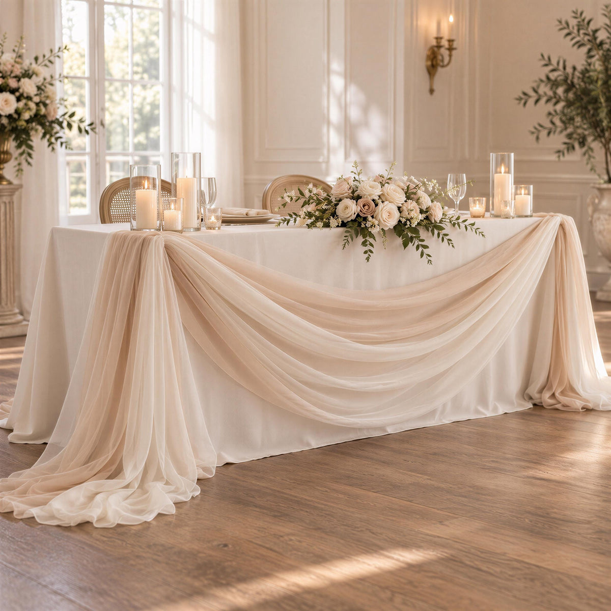 a beautifully decorated wedding reception table with a white tablecloth, draped with a flowing beige fabric. The table is adorned with a floral centerpiece and candles, creating a romantic and elegant atmosphere.