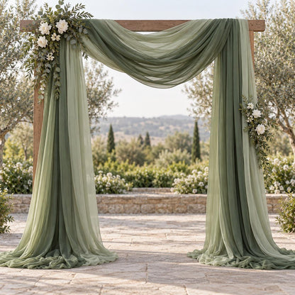 a beautifully decorated outdoor wedding arch with a lush green curtain and white flowers, set against a scenic backdrop of trees and a distant hill.