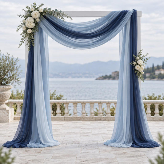 a beautiful wedding arch adorned with blue and white fabric, flowers, and greenery, set against a scenic backdrop of a body of water and mountains.