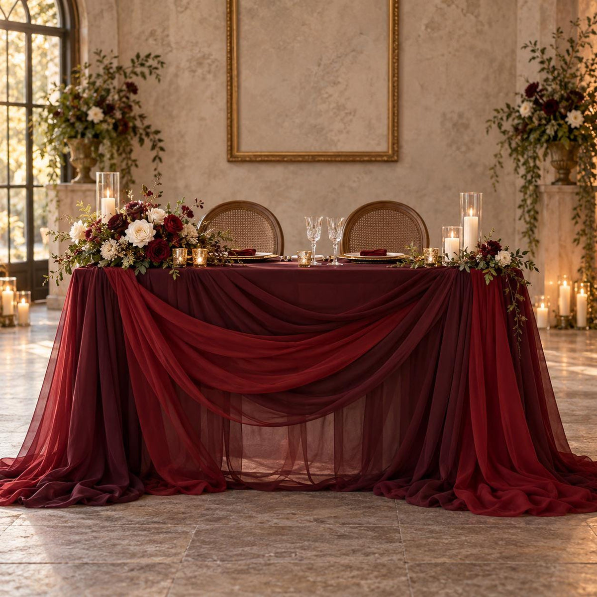 a beautifully decorated wedding reception table with a red tablecloth, white flowers, and candles. The table is set with two chairs and wine glasses, creating an elegant and romantic atmosphere.