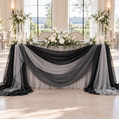 a beautifully decorated wedding reception table with a black and gray draped tablecloth, white flowers, and candles. The table is set with white plates and silverware, and the overall scene has a formal and elegant atmosphere.
