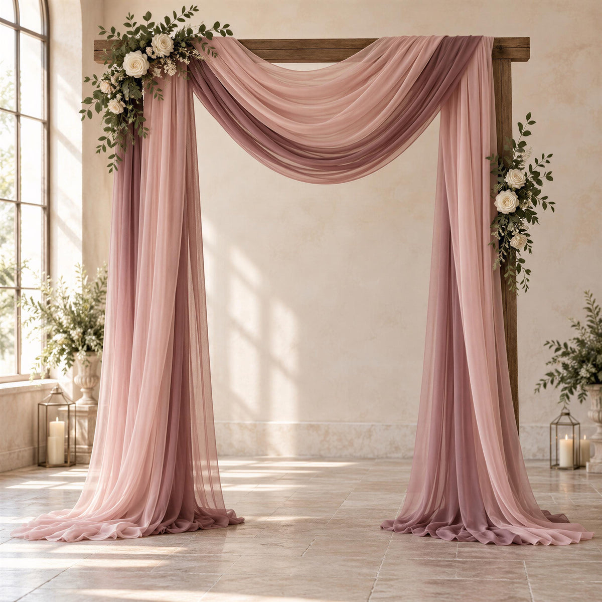 a beautifully decorated wedding arch with pink and purple drapes, adorned with white flowers and greenery. The arch is set against a backdrop of a white wall and a window, creating a serene and elegant atmosphere for a wedding ceremony.