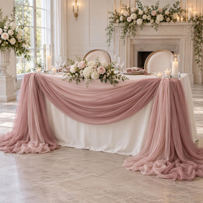 a beautifully decorated wedding reception table with a white tablecloth, pink and white floral arrangements, and a draped table runner. The table is set with wine glasses, plates, and candles, creating an elegant and romantic atmosphere.