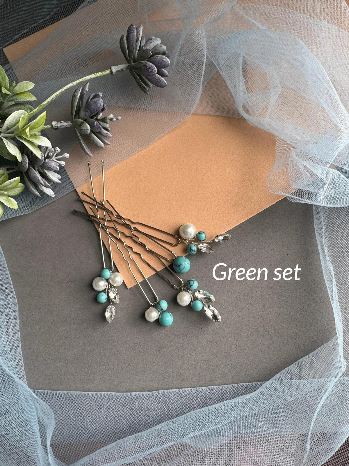 A collection of hair clips and beads arranged on a gray surface, with a white tulle fabric and some purple flowers in the background.