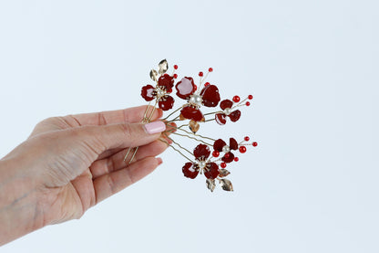 A hand holding a decorative hair clip with red flowers and red berries.