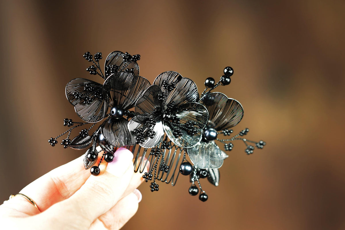 A hand holding a decorative hair accessory with black flowers and beads.