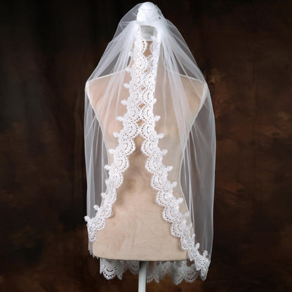 A mannequin wearing a white lace veil with a scalloped edge, displayed against a dark background.