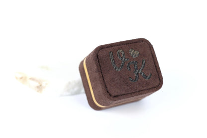 A brown, square-shaped jewelry box with the word "L" and a heart symbol printed on it.