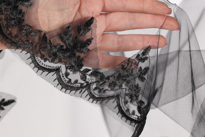 A hand is holding a piece of black lace with intricate floral embroidery.