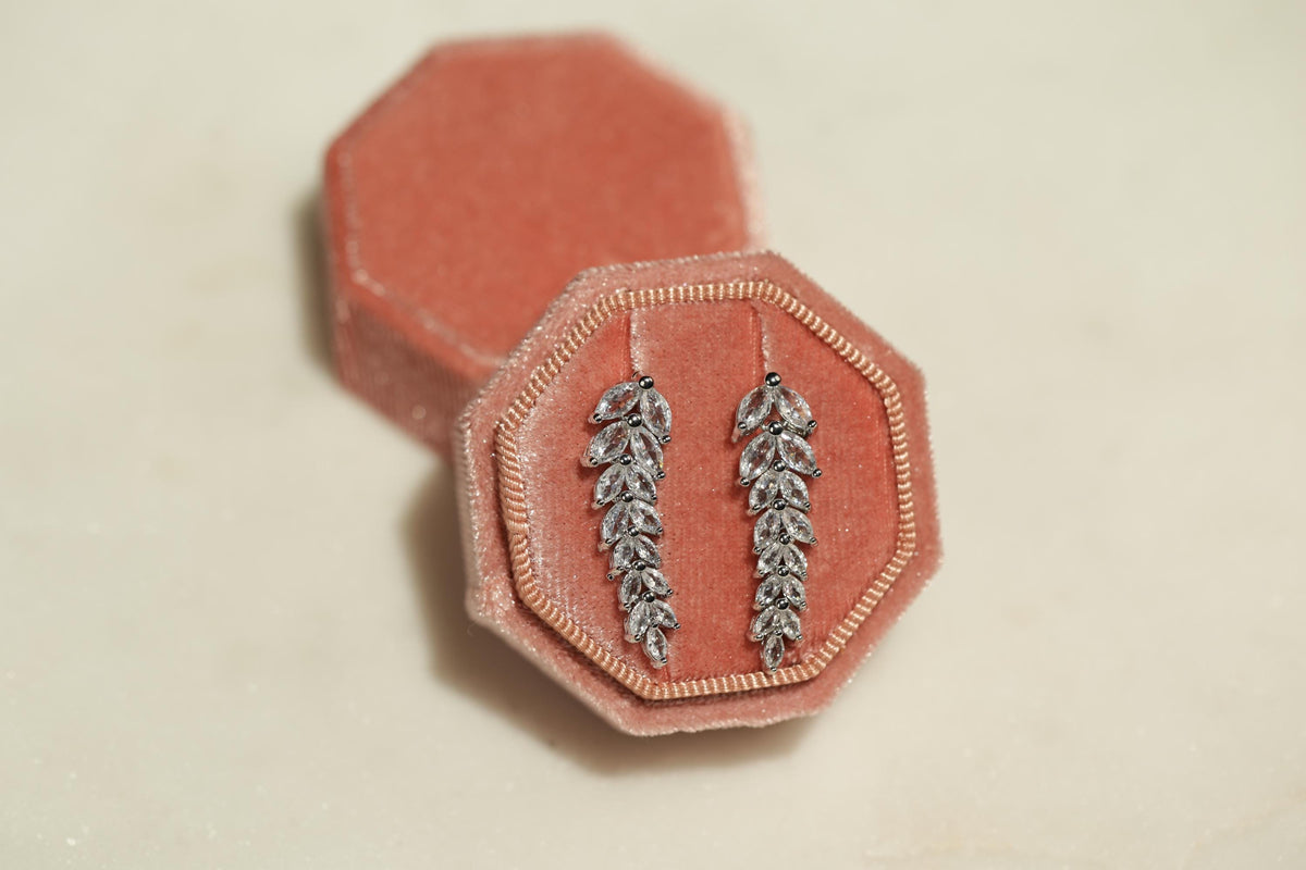 A pair of silver earrings with leaf-shaped designs, displayed in a pink velvet jewelry box.