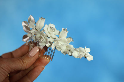 A hand holding a decorative hair accessory with white flowers against a blue background.