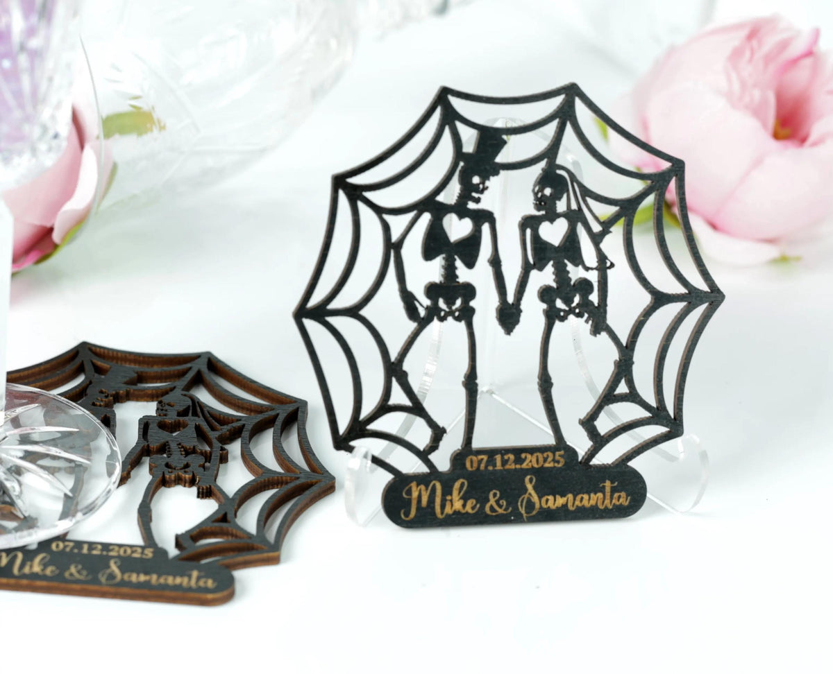 a couple of custom-made wedding or anniversary decorations, including a spider web-like design and a wooden frame with a couple's silhouette. The decorations are placed on a white surface, with a pink flower in the background.
