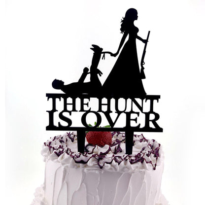 a cake with a silhouette of a woman holding a rifle and the text "THE HUNT IS OVER" on the cake topper.