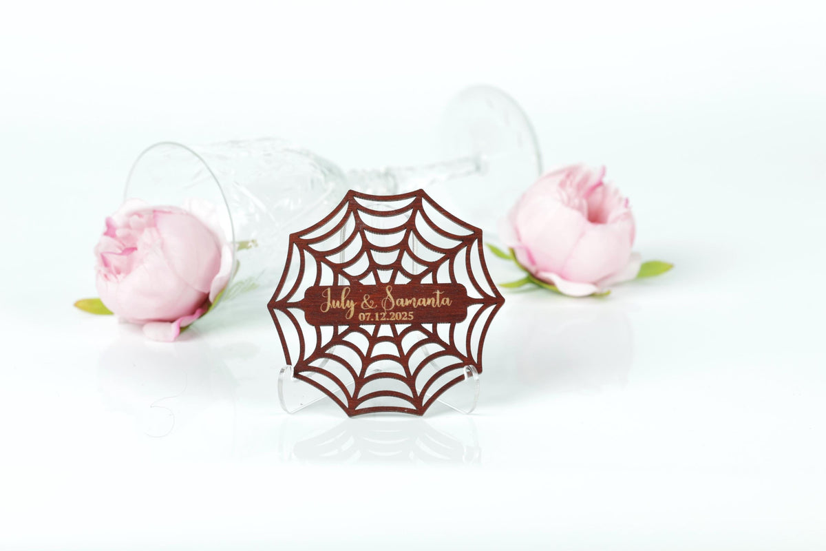 a wooden spider web-shaped label with the text "July & Santo" and "07.12.2015" on it, placed in front of two pink roses.