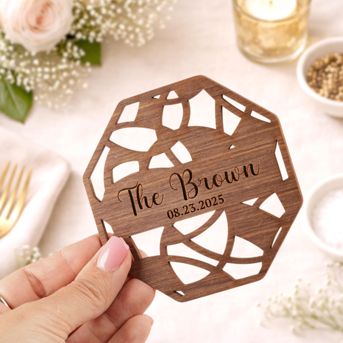 A hand holding a wooden coaster with the text "The Brown" and the date "08.23.2025" printed on it.