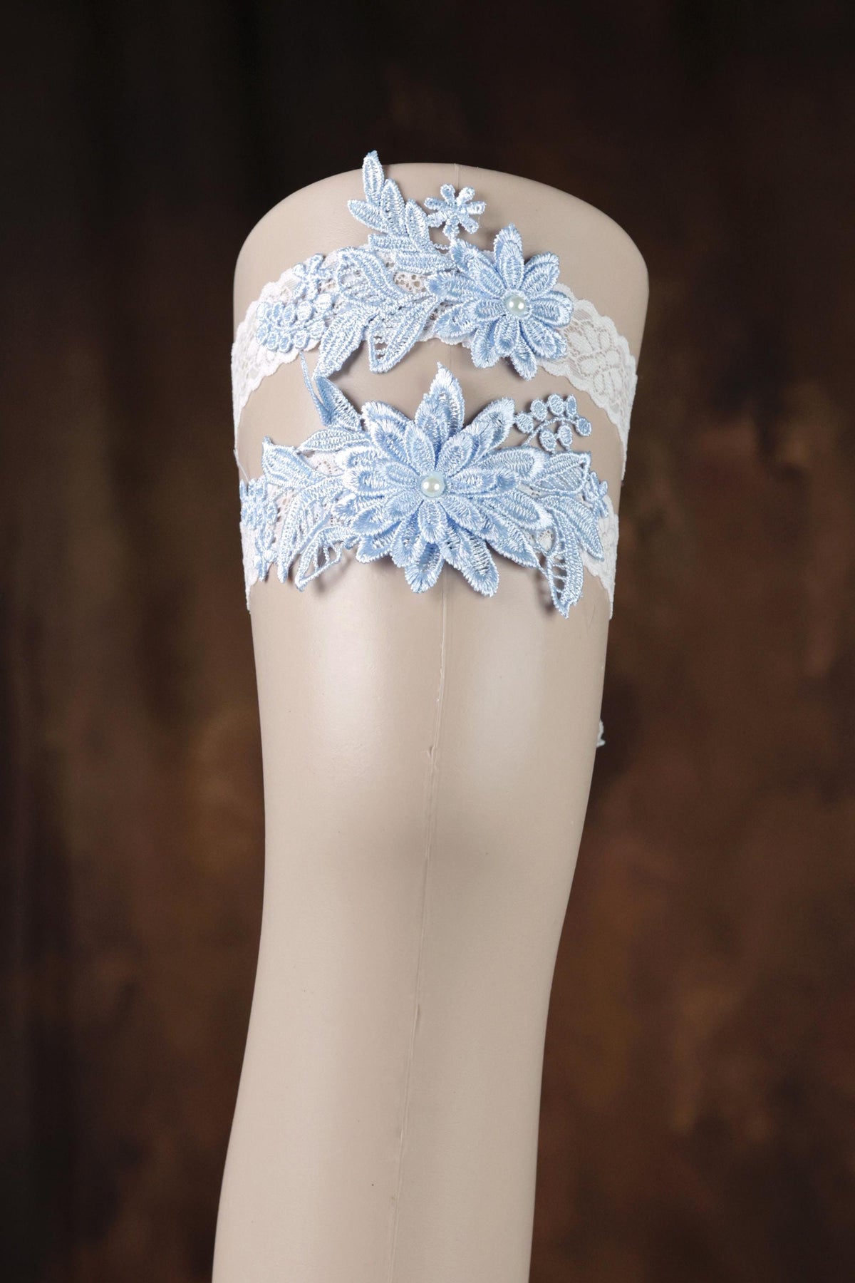 A mannequin leg wearing a white lace garter belt with blue floral designs.