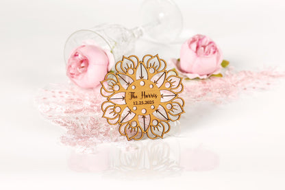 a wooden ornament with a floral design, placed on a white surface alongside two pink roses and a glass of wine.