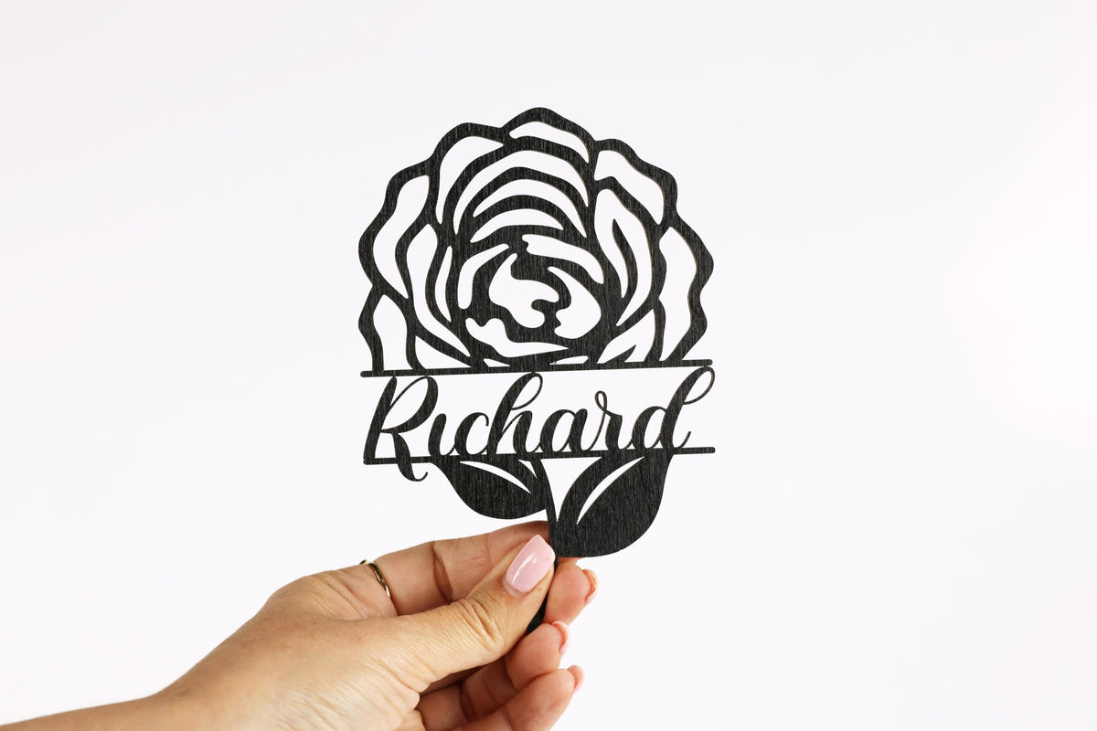 A hand holding a black and white cutout of a rose with the name "Richard" written below it.