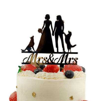 A white wedding cake with a black silhouette of a bride and groom on top, along with a "Mrs & Mrs" sign.