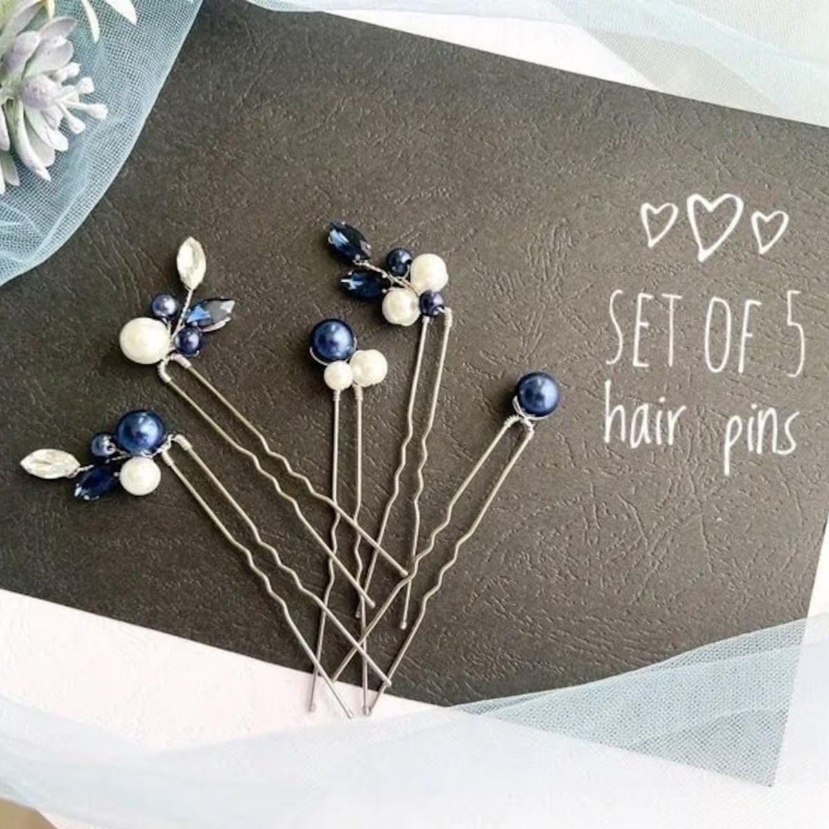 A set of five hair pins with blue and white beads, arranged on a black background.