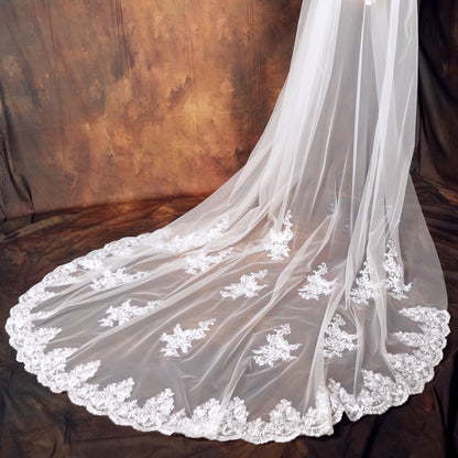 A white wedding veil with intricate lace detailing and a flowing, cascading shape.