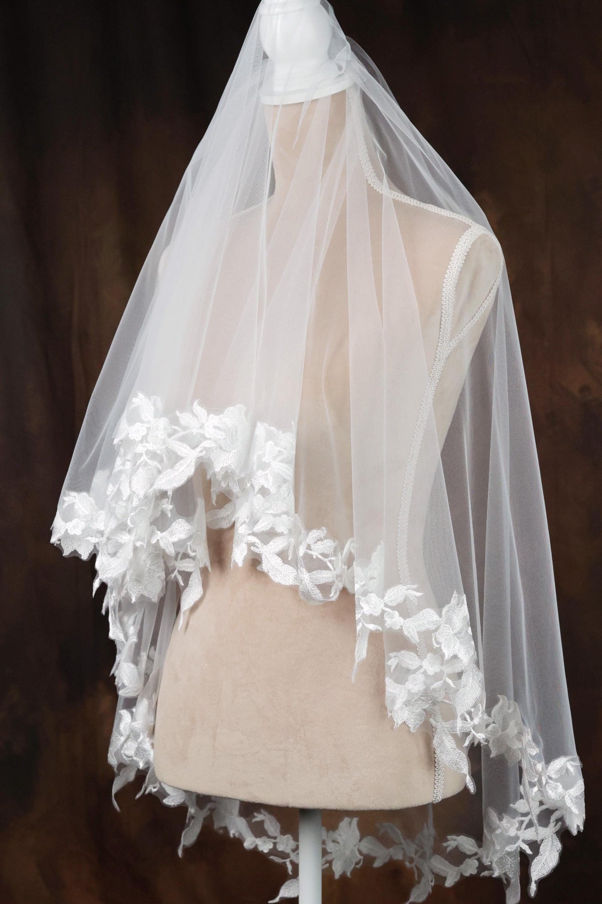 A white wedding veil with a delicate lace trim is displayed on a mannequin.