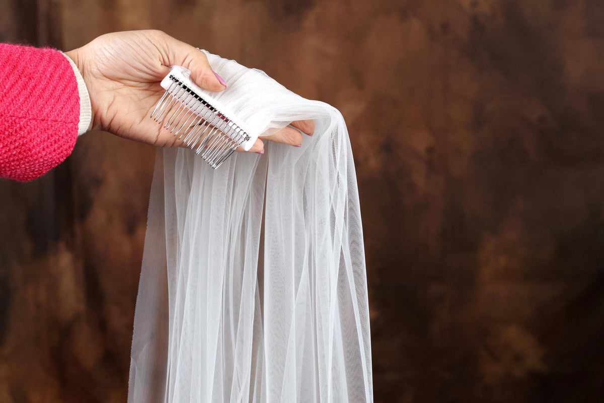 A hand holding a white veil against a brown background.
