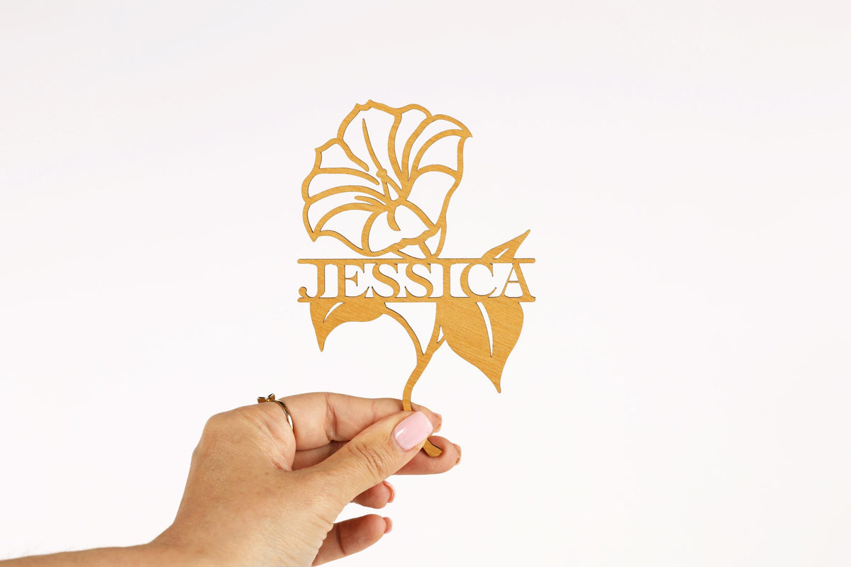 A hand holding a gold-colored paper cutout of a flower with the name "JESSICA" written on it.