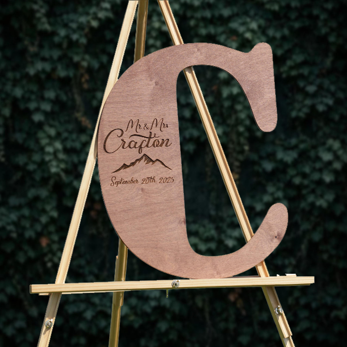 A wooden letter 'C' on a stand, with the text "Mr & Mrs Crafton September 20th 2023" engraved on it.