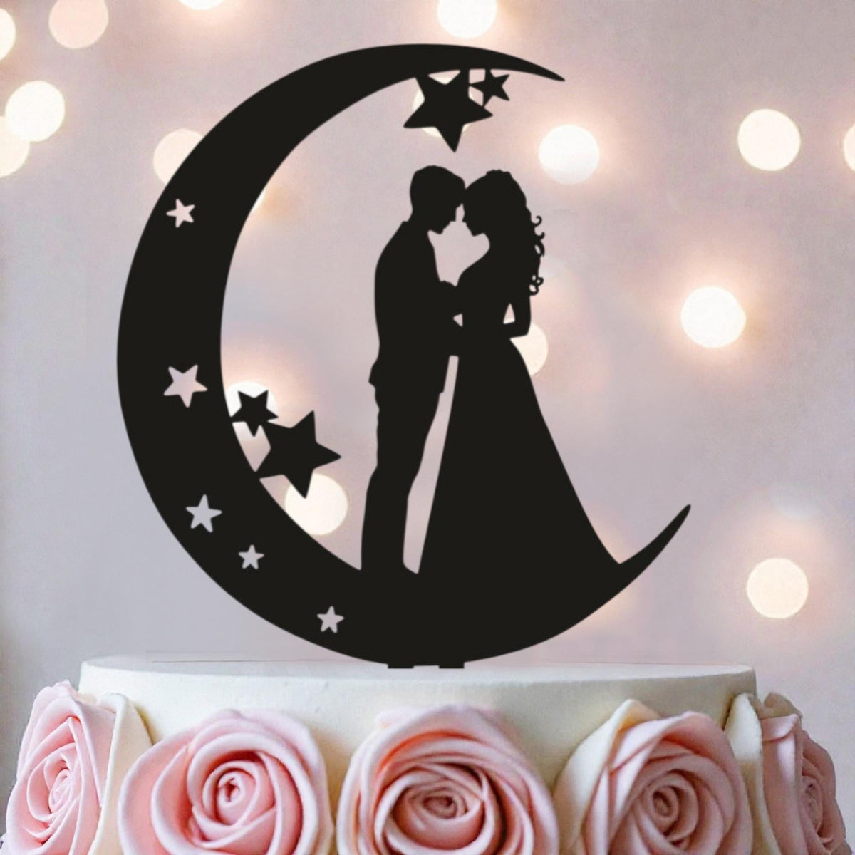 A silhouette of a couple embracing under a crescent moon with stars, serving as a wedding cake topper.