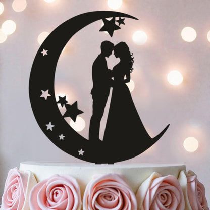 A silhouette of a couple embracing under a crescent moon with stars, serving as a wedding cake topper.