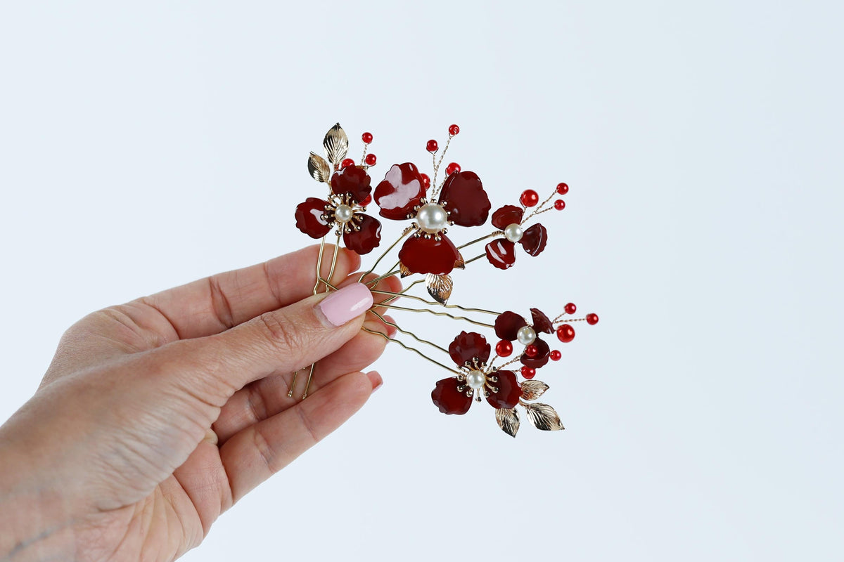 A hand holding a decorative hair clip with red flowers and red berries.
