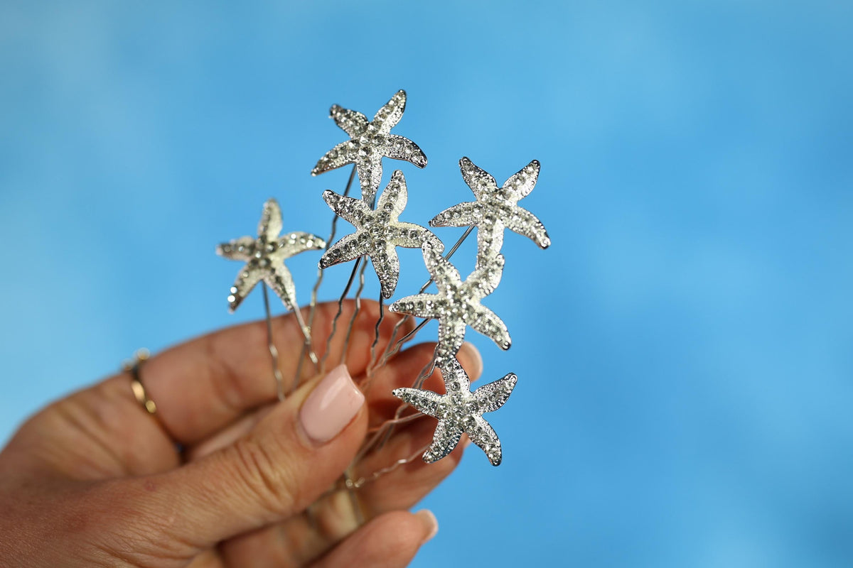 A hand holding a group of silver star-shaped hair clips against a blue background.