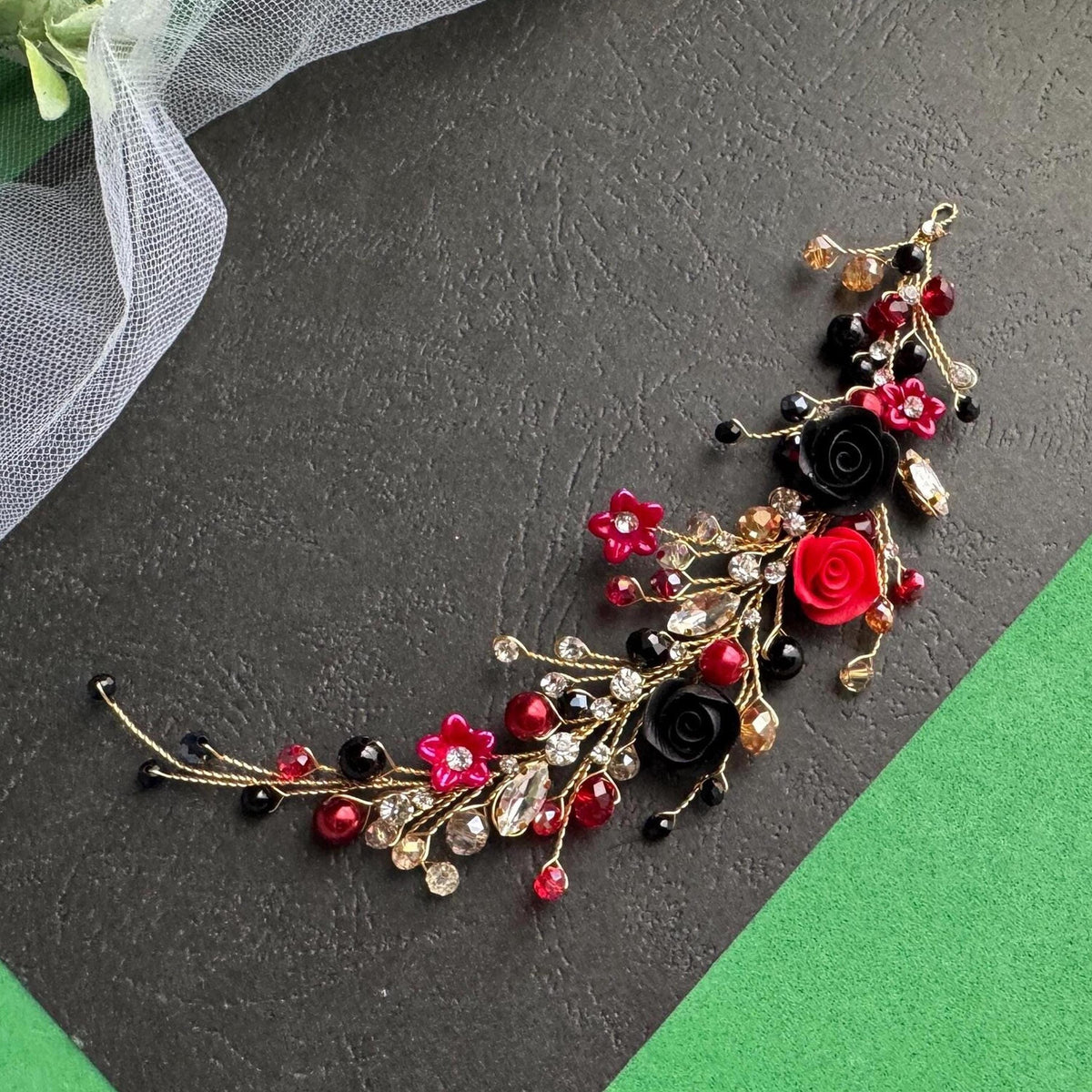 A decorative piece of jewelry with a combination of red, black, and gold elements, including flowers, beads, and gemstones, arranged on a black surface.