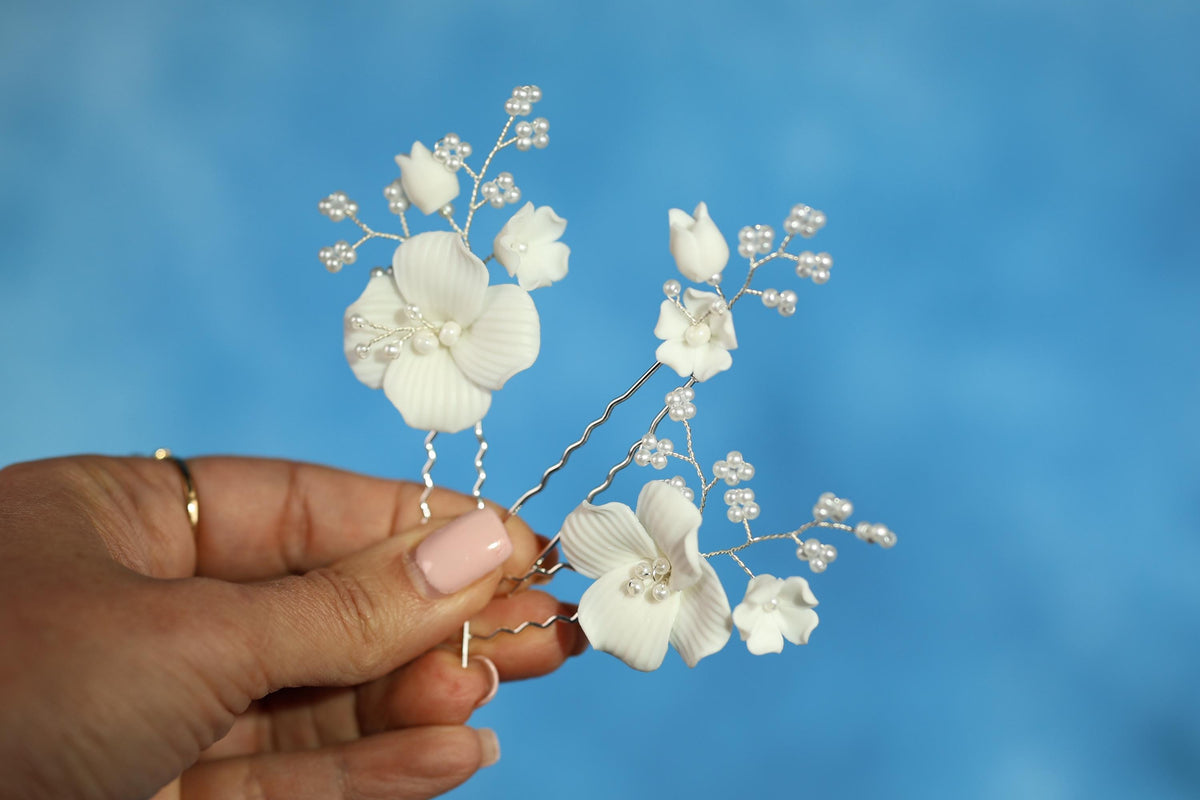 A hand holding a pair of white flower-shaped hair clips against a blue background.