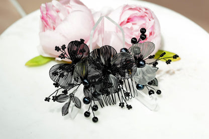 A decorative hair accessory with black and white floral elements, including a black and white floral pattern and black pearls, placed on a white surface.