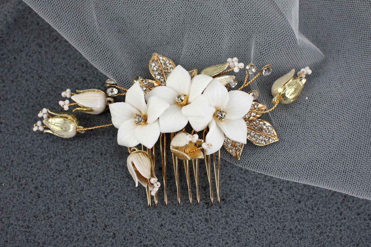 A decorative hair clip with white flowers and gold accents, placed on a gray surface.