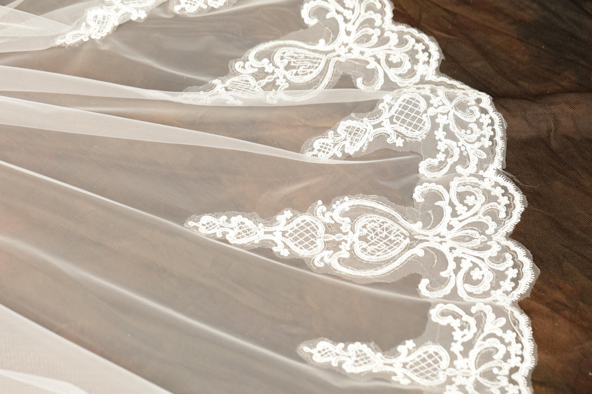 A close-up view of a delicate white wedding veil with intricate lace and floral embroidery.