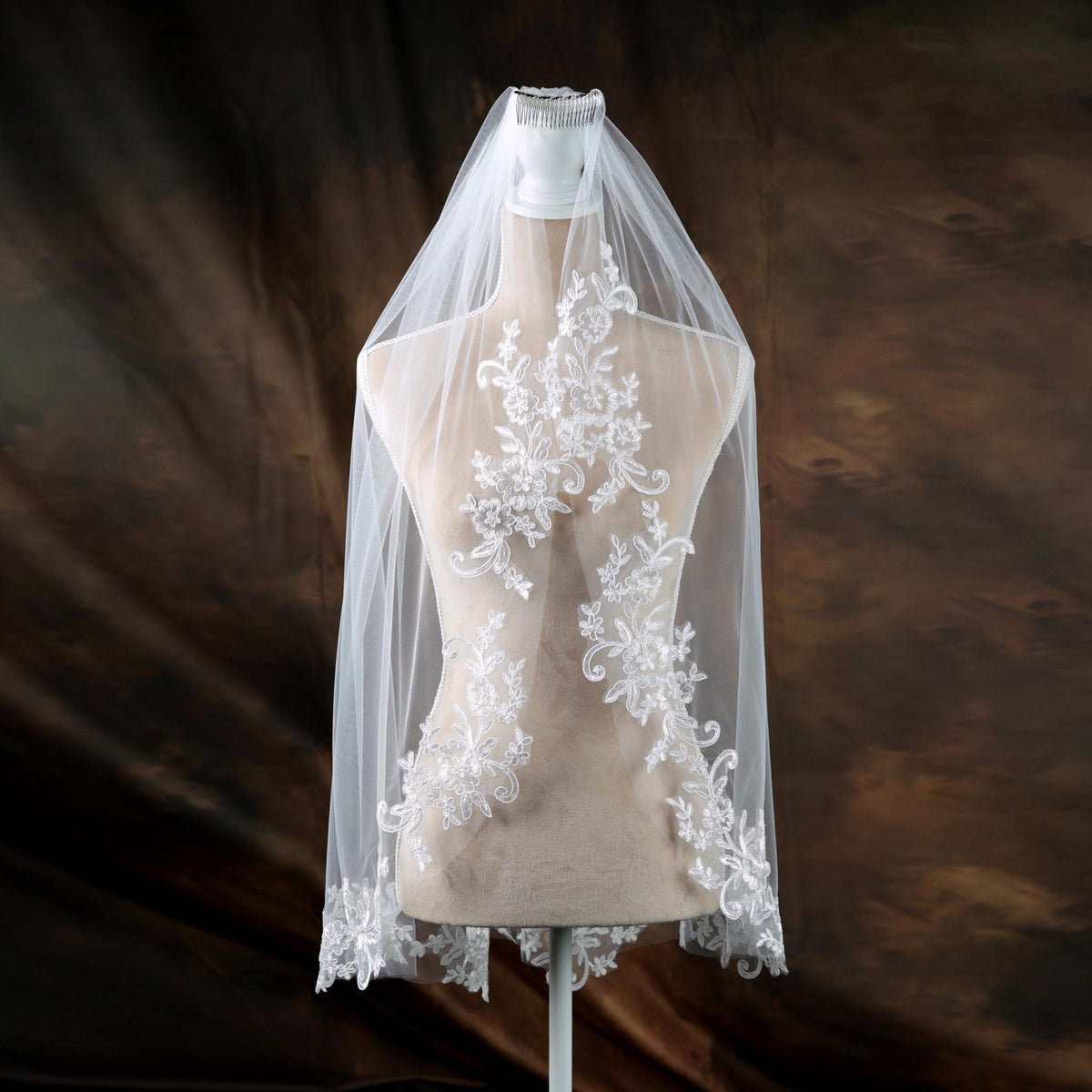 A mannequin wearing a white wedding veil with intricate lace detailing.