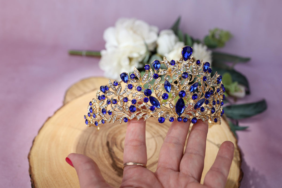 a woman's hand holding a blue and gold tiara