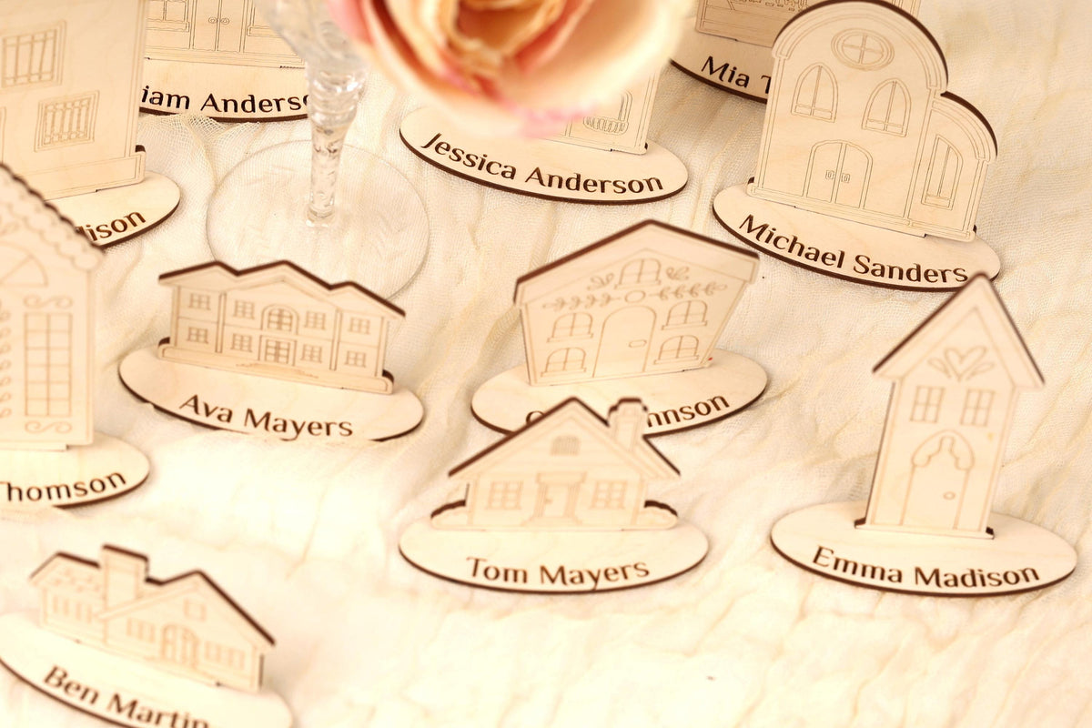 a collection of wooden house-shaped place cards, each with a name on it, arranged on a white surface.