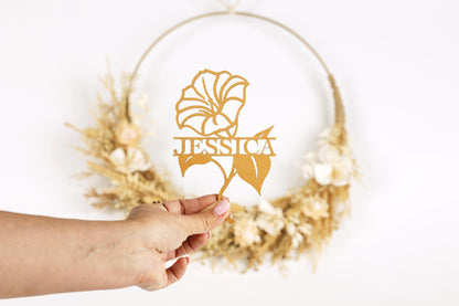 A hand holding a piece of paper with a gold flower design and the name "JESSICA" written on it.