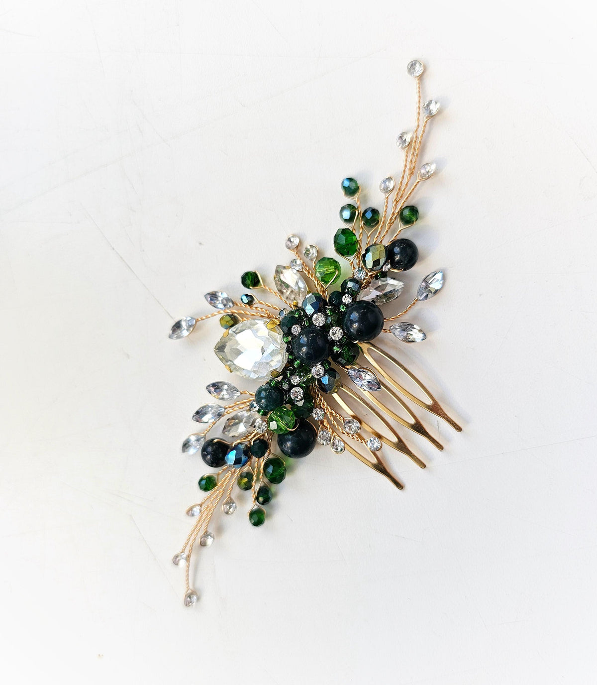 A decorative hair accessory with a gold-colored comb and various colorful gemstones, including green and white stones, as well as some larger, clear gemstones.
