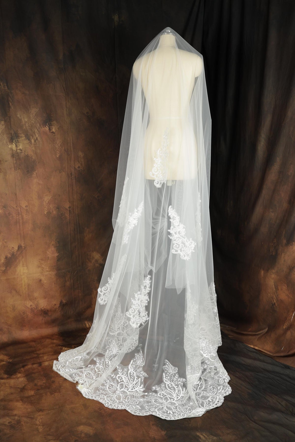 A white lace veil with intricate floral embroidery is displayed against a brown background.